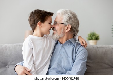 Happy grandfather sit on couch enjoy spending time with preschooler grandson at home, loving smiling grandparent and little boy child relax on sofa have close tender moment touch noses look in eyes