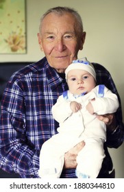 Happy Grandfather With Small Cute Baby Grandson Posing At Home Looking Ahead. Concept Of Two Generation Family. Everyday Joy Lifestyle Without Age Limitation.