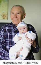 Happy Grandfather With Small Cute Baby Grandson Posing At Home Looking Ahead. Concept Of Two Generation Family. Everyday Joy Lifestyle Without Age Limitation.