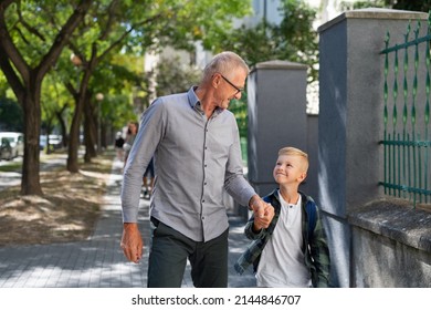 Happy grandfather taking his grandson home from school, walking outdoors in street. - Powered by Shutterstock