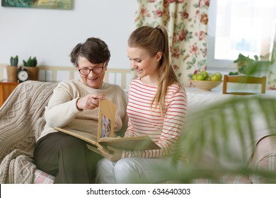 Happy grandma and granddaughter sitting on a sofa and watching family photo album - Powered by Shutterstock