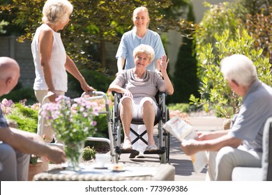 Happy grandma in wheelchair waving to her friend with walking frame during free time in garden - Powered by Shutterstock