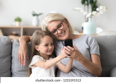 Happy grandmother and cute granddaughter using cellphone together, smiling older grandma and child girl having fun taking selfie on phone, cheerful granny with little kid play making photo on mobile - Powered by Shutterstock