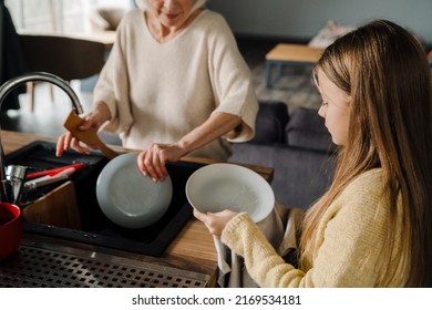 Happy grandmother and granddaughter washing dishes together in kitchen at home - Powered by Shutterstock