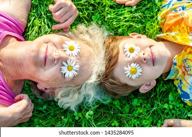 Happy  Grandmother With Grandson Having Fun Lying On The Lawn With Daisies On Their Eyes. Summer Vacation With My Grandmother.  