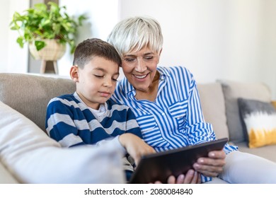 Happy grandmother and grandson using tablet together, sitting on cozy sofa at home, browsing tablet device apps, grandma with grandchild playing game, looking at screen, having fun - Powered by Shutterstock