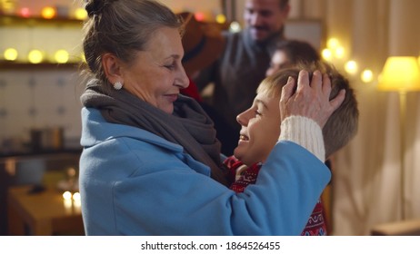 Happy Grandmother Hugging Little Boy Visiting On Christmas Eve. Multigenerational Family Gathering Together In Decorated Apartment Celebrating New Year