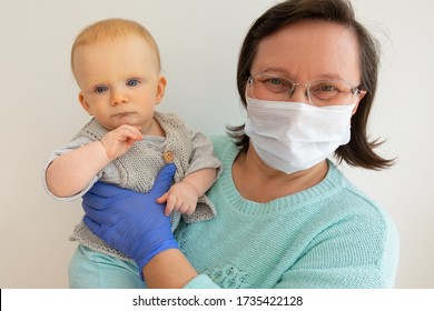 Happy Grandmother In Medical Mask And Gloves Enjoying Time With Baby Granddaughter. Mature Woman With Little Child Posing Isolated Against White Background. Babysitting And Virus Guidance Concept