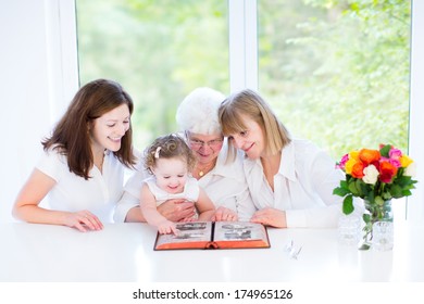 Happy Grandmother Watching Black And White Photo Album With Her Daughter And Grandchildren In A Beautiful White Dining Room With A Big Garden View Window