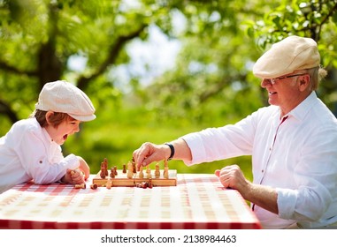 glücklicher Großvater und Enkel, der Schach im Frühjahrsgarten spielt