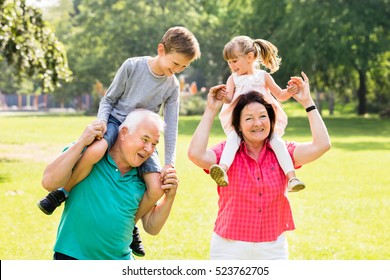 Happy Grandparents Giving Fun Piggyback Ride To Their Grandchildren In Park