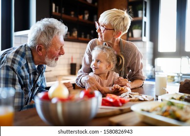 Happy Grandparents With Grandchildren Making Breakfast In Kitchen