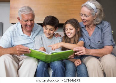 Happy Grandparents And Grandkids Looking At Album Photo In The Living Room