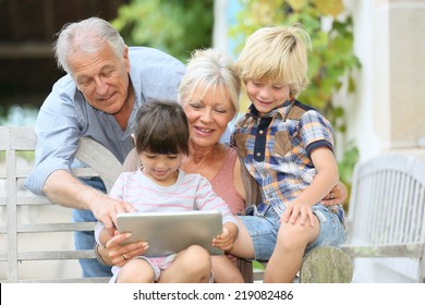 Happy Grandparents Playing Game On Tablet With Kids