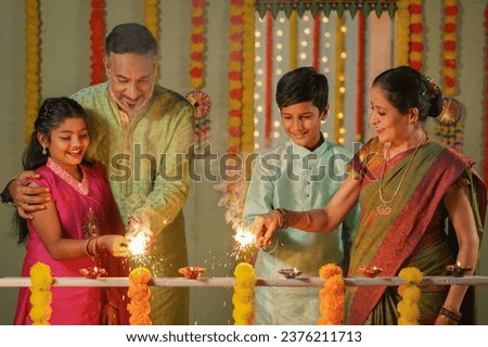 Happy Grandparents playing with sparklers or Crackers with Kids near balcony at home during diwali festival celebration - concept of Traditional culture, Familt generation and Caring family