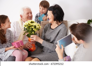 Happy Grandparents Receiving Flowers And Presents From Their Lovely Grandchildren