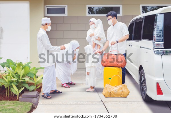 Happy grandparents\
wearing face mask while visited by their family during Eid Mubarak\
and standing next to a\
car