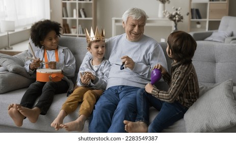 Happy grandson kid and multiethnic friends playing with positive grandpa, using musical toys, crown for role games, resting on sofa, talking, laughing, enjoying leisure, playtime, daycare activities - Powered by Shutterstock