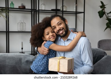 Happy grateful dad hugging adorable teen daughter girl, holding festive surprising gift due to fathers day, birthday, looking at camera, smiling. Fatherhood, family concept. Head shot portrait