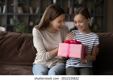 Happy grateful girl giving mothers day gift to mom, holding pink present box. Excited millennial mum and cute daughter kid celebrating birthday, hugging on couch at home, going to unpack festive wrap - Powered by Shutterstock