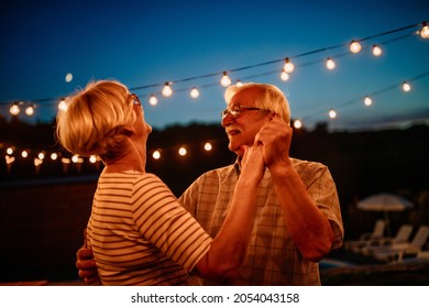 Happy Gray Haired Senior Retired Couple, Dancing Outdoors. Smiling Elder Man And Woman Enjoying Evening In The Backyard. Family Outdoors Lifestyle