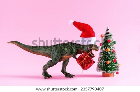 Happy green dinosaur in Santa Claus hat hold present box on pink background.
