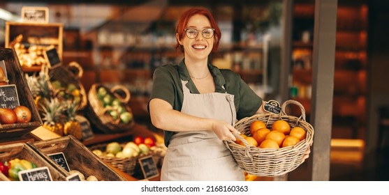 Happy grocery store owner smiling at the camera while holding a basket of fresh organic grapefruits. Successful female entrepreneur running a small business in the food industry. - Powered by Shutterstock