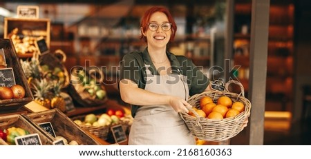 Happy grocery store owner smiling at the camera while holding a basket of fresh organic grapefruits. Successful female entrepreneur running a small business in the food industry.