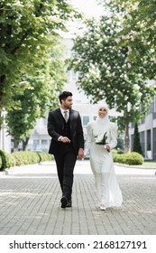 happy groom holding hands with muslim bride with wedding bouquet and walking together