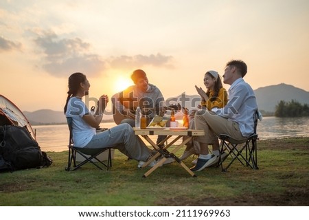 happy group of Asian friends Play guitar and sing enjoying camping and drinking beer