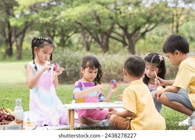 Happy group of cute little children girls painting Easter eggs together. Diverse kids holding painting brush, painting watercolor on egg while playing outdoors at park - Powered by Shutterstock