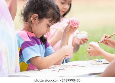 Happy group of cute little children girls painting Easter eggs together. kids holding painting brush, painting watercolor on egg while playing outdoors at park - Powered by Shutterstock