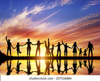 Happy group of diverse people, friends, family, team standing together holding hands and celebrating success. Water reflection, sunset sky