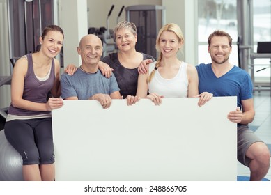 Happy group of elderly and young people at the gym holding a big blank white placard with copyspace for your text - Powered by Shutterstock