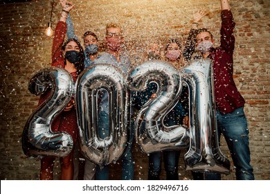 Happy Group Of Friends With Face Mask Celebrating New 2021 Year - Confetti Falling In The Air - Young People With Balloons In Hands Making New Year Party At Home - Focus On Balloons.