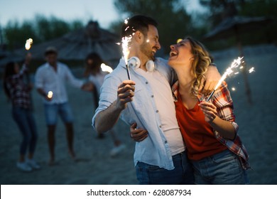 Happy group of friends lighting sparklers and enjoying freedom at beach during sunset - Powered by Shutterstock