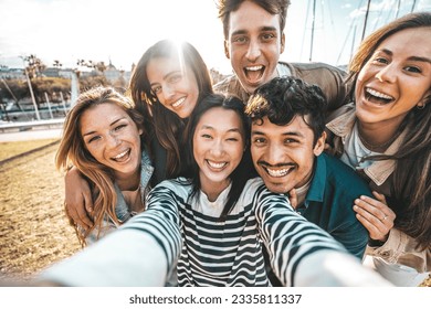 Happy group of friends taking selfie pic with smart mobile phone device  - Diverse young people enjoying sunny day out - Life style concept with guys and girls hanging outside together - Shutterstock ID 2335811337