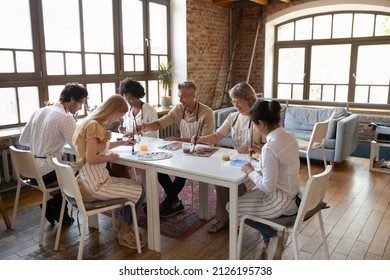 Happy group of motivated multigenerational diverse people sitting together at table, involved in drawing pictures with paintbrushes, enjoying taking part in creative art master class in modern studio. - Powered by Shutterstock