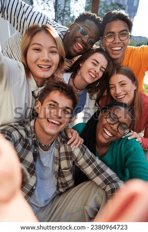 Happy group of multiethnic classmate taking a selfie together outdoors in the university campus, looking at camera cheerfully raising arms, celebrating last day. Vertical photo.