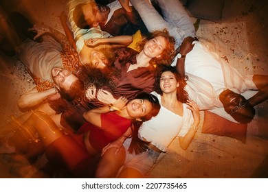 Happy group of multiracial friends lying down on the floor at night at a private after-party. They are tipsy and happy to be together.