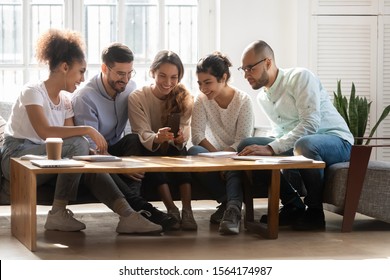 Happy group of multiracial students chilling together on comfortable couch at home. Smiling young mixed race girl holding smartphone, showing funny photos to friends, recording video or holding call. - Powered by Shutterstock