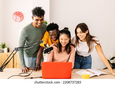 Happy group of multiracial young student friends working together recording radio podcast using microphone and laptop at home office. Teamwork and community concept with diverse people live streaming