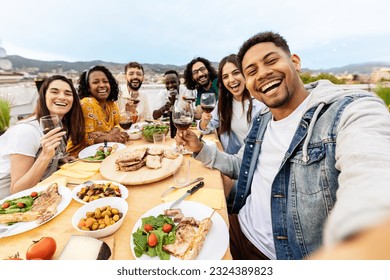 Happy group of people toasting red wine at eatery barbecue lunch party. Multiracial friends taking selfie portrait together enjoying food and drink at summer celebration. Friendship concept