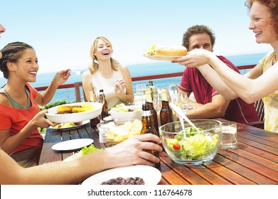 A Happy Group Of Teenage Friends Sitting At A Table At The Seaside Drinking Beer And Eating Their Lunch