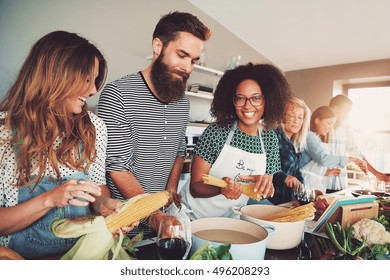 Happy group of young adult men and women cooking together at home in small kitchen or culinary classroom - Shutterstock ID 496208293