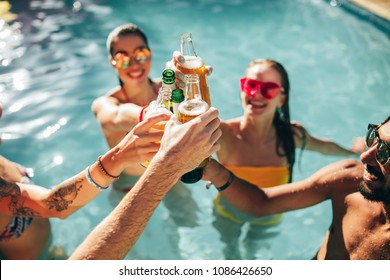 Happy group of young people in swimming pool drinking beers. Multiracial friends enjoying and toasting drinks during a pool party. - Powered by Shutterstock