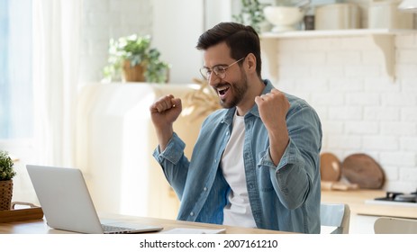 Happy guy celebrate great news opportunity got read by e-mail. Excited man sit in kitchen look at laptop screen with clenched fists feels incredible amazed received good notice. Sale, discount concept - Shutterstock ID 2007161210