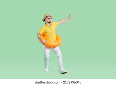 Happy Guy Going On Summer Holiday At Seaside. Full Body Length Of Funny Cheerful Man In Yellow T Shirt, Hat, Sunglasses And Orange Inflatable Ring Waving Goodbye Isolated On Light Green Background