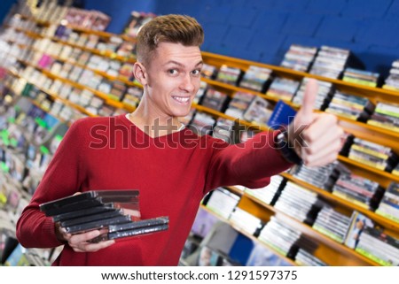 Happy guy holding stack of DVDs bought in shop giving thumbs up
