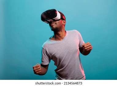 Happy guy playing online game with virtual reality glasses in front of camera. Young adult using vr headset with 3d futuristic simulation and interactive vision, enjoying visual innovation.